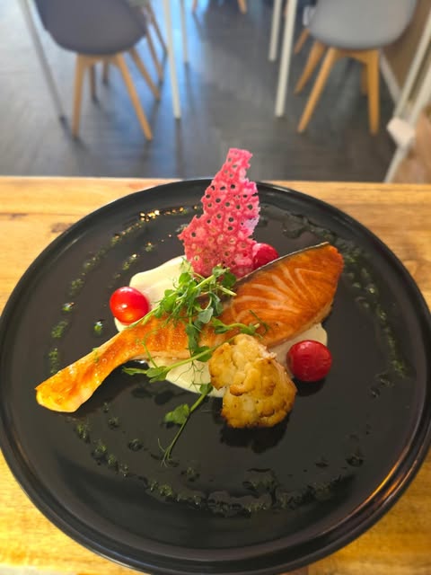 Pavé de saumon snacké, crème, tuile rose et petites tomates sur une assiette noire